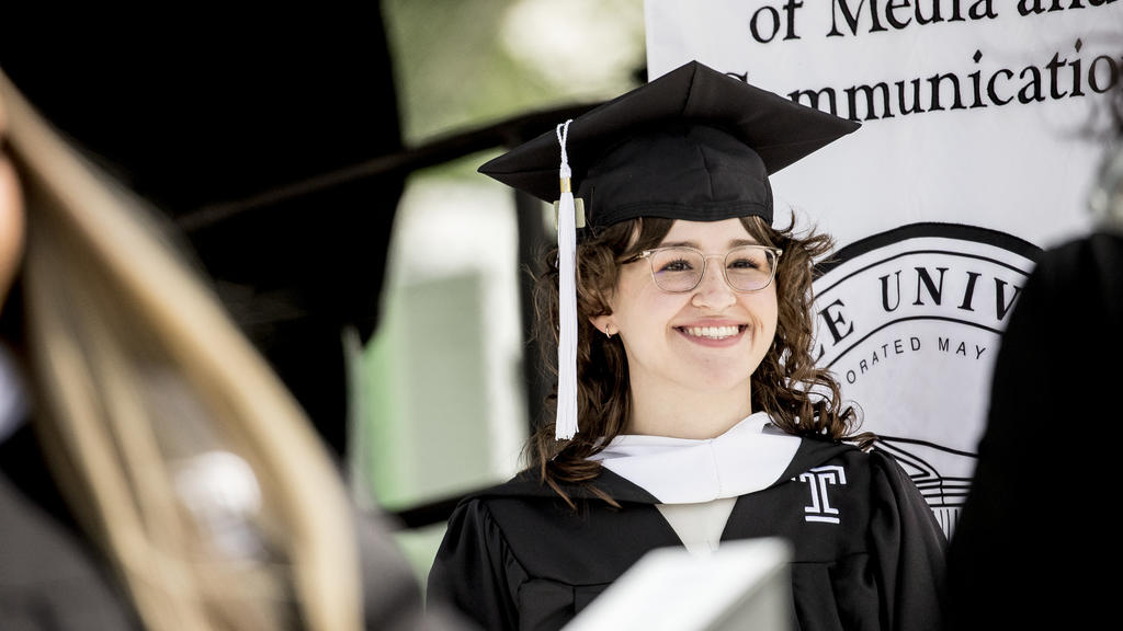 An image of a smiling graduated student on stage at commencement. 