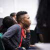 Male student wearing a red lanyard listens attentively in class