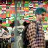 A young man with green hair is standing in a cafeteria filled with students and with a wall of country flags behind them.
